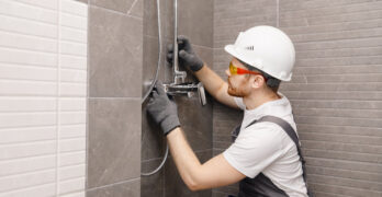 Plumber installing water taps shower stall, work in bathroom